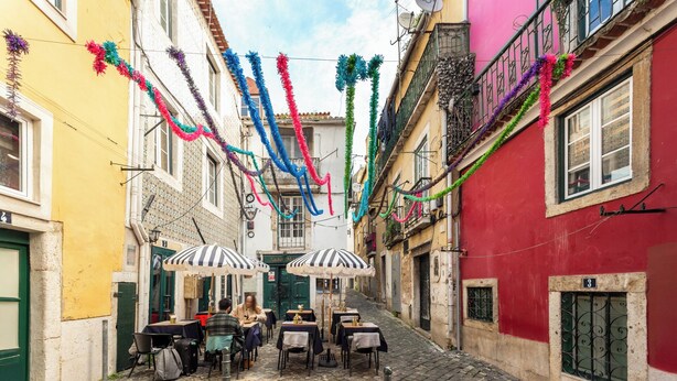 Una estrecha calle adoquinada con mesas y sillas en la calle, decorada con serpentinas de colores.