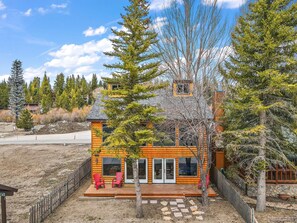 A log cabin with a deck, two red Adirondack chairs, and a stone pathway leading to the entrance.