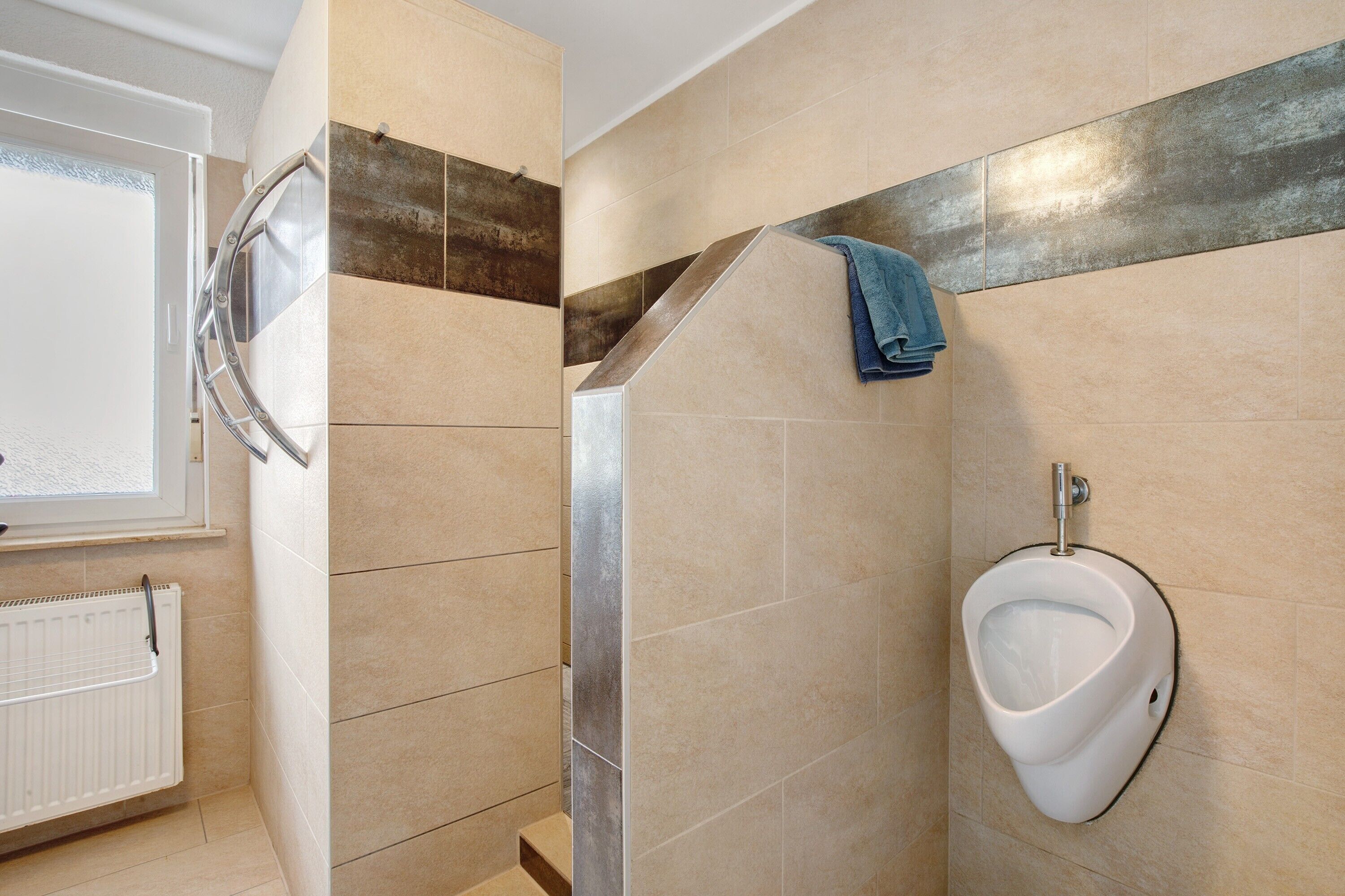 A bathroom with a urinal, a towel rack, and a window.