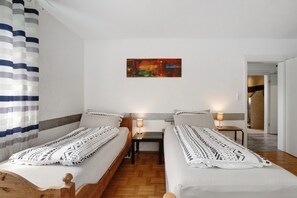 Una habitación con dos camas, una mesita pequeña, un cuadro colgado en la pared y una puerta que da a otra estancia.