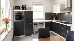 Une cuisine moderne avec un coin repas, comprenant un four encastré, un four à micro-ondes et une machine à café, et dotée d’une fenêtre qui laisse entrer la lumière naturelle.
