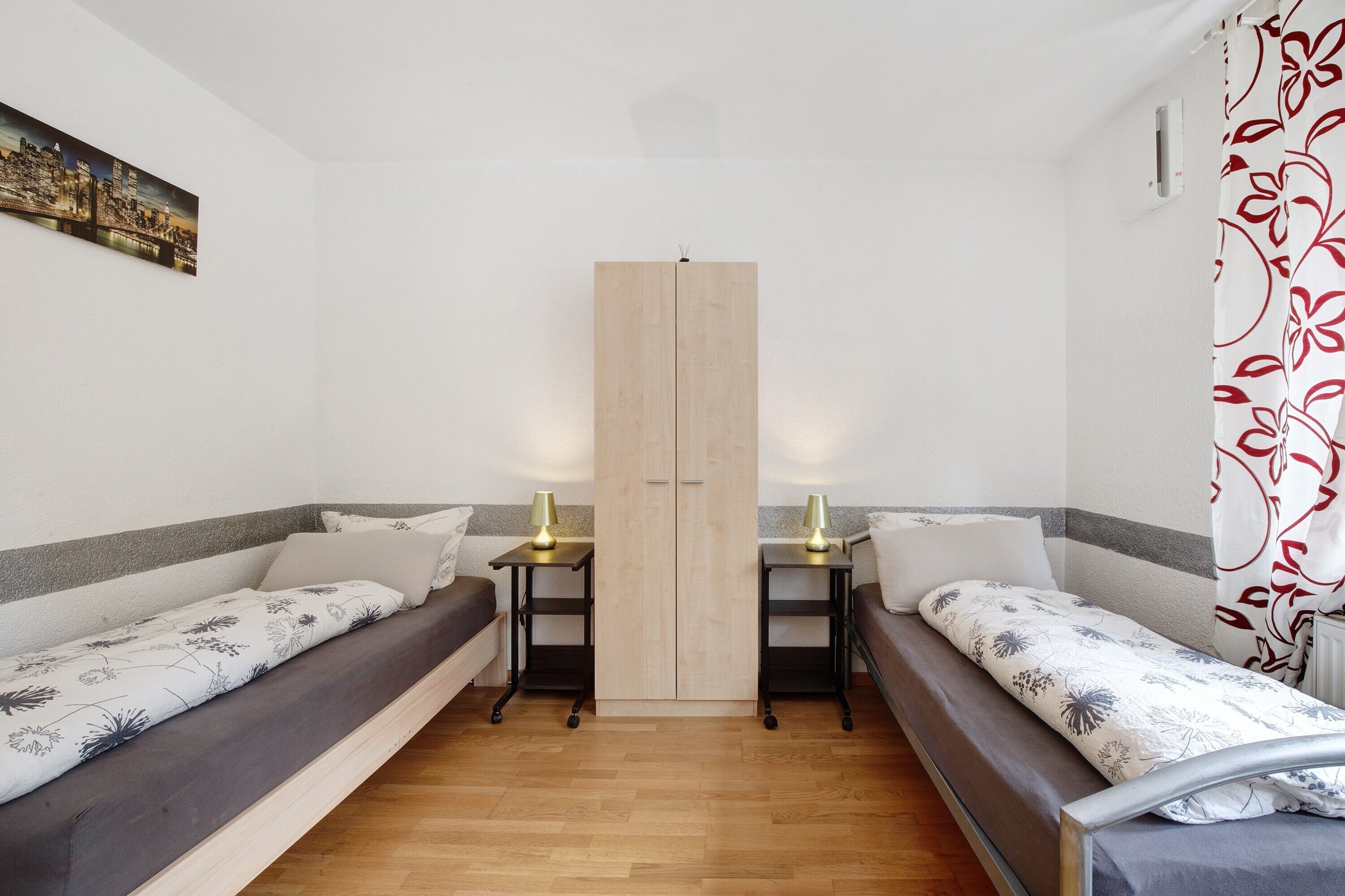 A room with two single beds, a wardrobe, and a small table with a lamp.