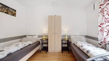 A room with two single beds, a wardrobe, and a small table with a lamp.