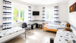 Une chambre avec deux lits, un bureau, une chaise, une télévision et une fenêtre avec des rideaux.
