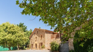 Un edificio de piedra con un patio, una puerta de madera y un árbol grande que da sombra.
