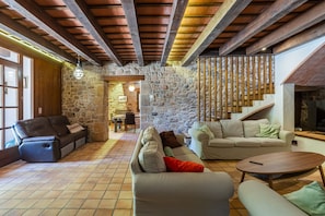 A spacious living area with stone walls, wooden beams, and a fireplace. - Can Pla - Disconnect to Connect (Sant Hilari Sacalm)