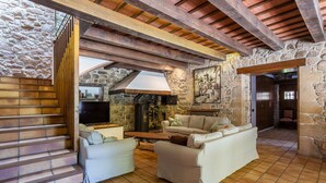 A rustic interior with a stone wall, wooden beams, a fireplace, and a staircase.