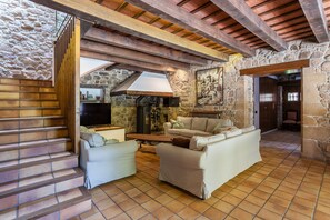 Um interior rústico com parede de pedra, vigas de madeira, lareira e escada.
