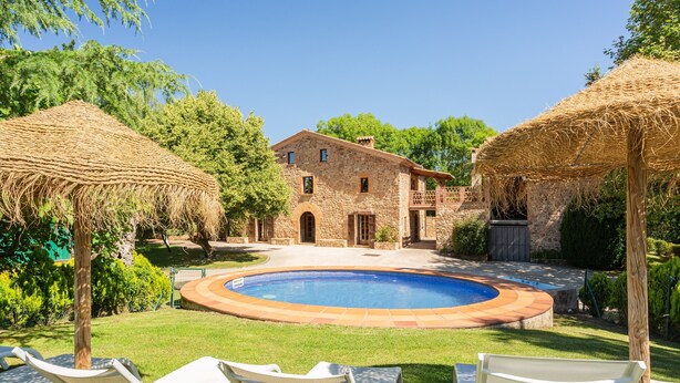 Una casa de piedra con piscina, rodeada de césped y árboles.