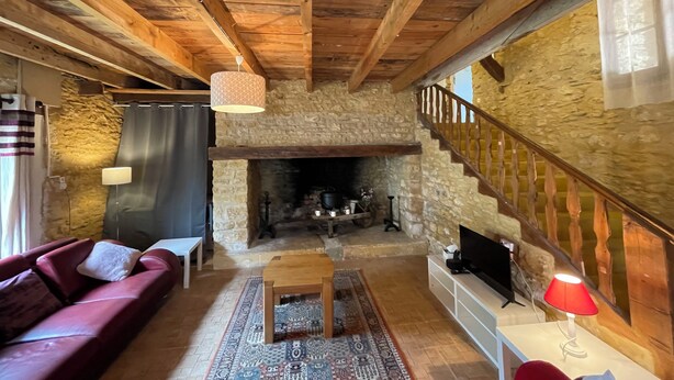 Una sala de estar rústica con chimenea de piedra, vigas de madera, un sofá rojo y una escalera.