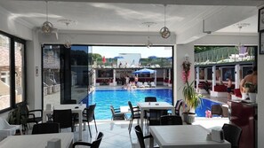 A poolside area with tables and chairs, a pool, and a view of the pool area. - buseyine otel (Marmara)