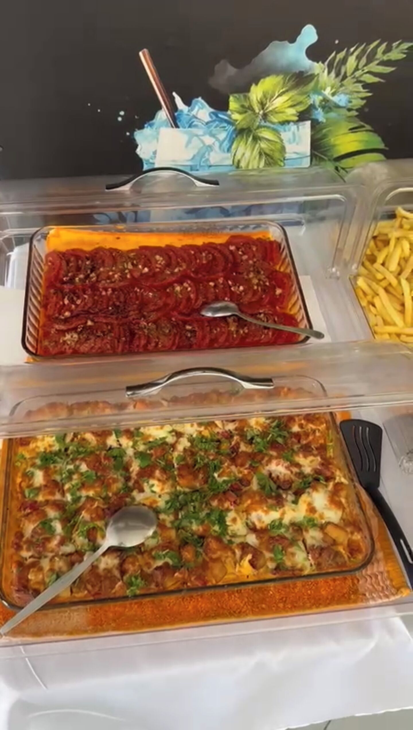 Une table de buffet avec trois plats en verre contenant différents mets, une cuillère et une fourchette.