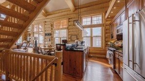 L’intérieur d’une cabane en rondins, avec un escalier en bois, une cuisine équipée d’appareils électroménagers en acier inoxydable et de grandes fenêtres.