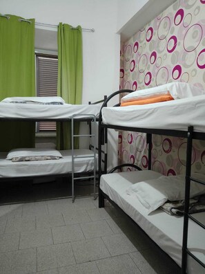 Una habitació de dormitori amb lliteres, una finestra amb persianes i una cortina.