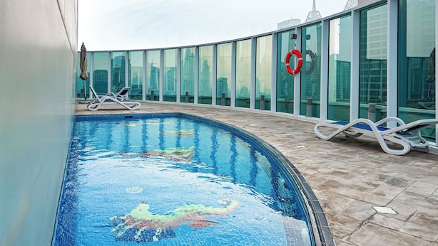 A swimming pool with a cityscape view, lounge chairs, and a lifebuoy. - PVH - Sunny Studio - Madison Residency (Dubai)