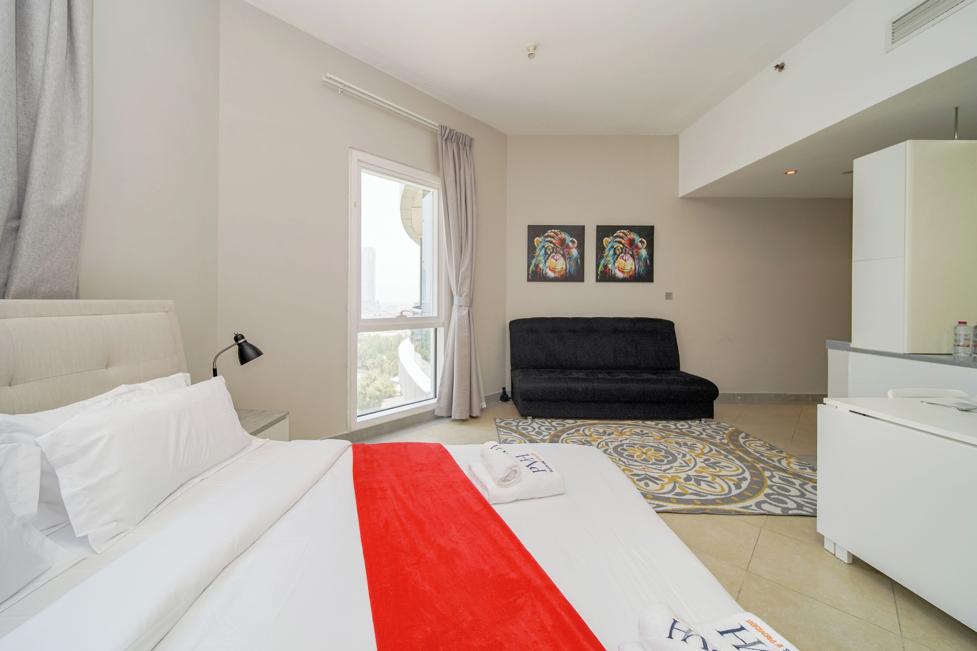 Habitación de hotel con cama, escritorio, silla, ventana y dos cuadros en la pared.