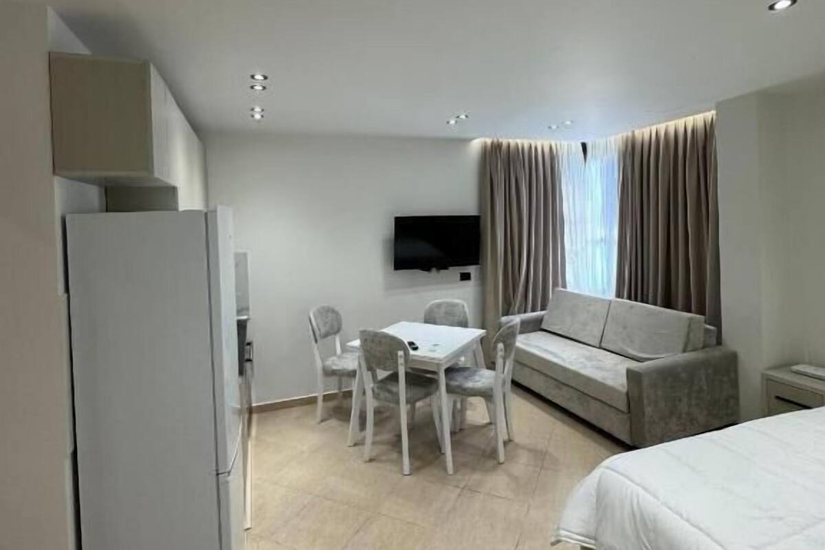 Une chambre d’hôtel moderne équipée d’un lit, d’un bureau avec des chaises, d ’une télévision et d’un réfrigérateur.