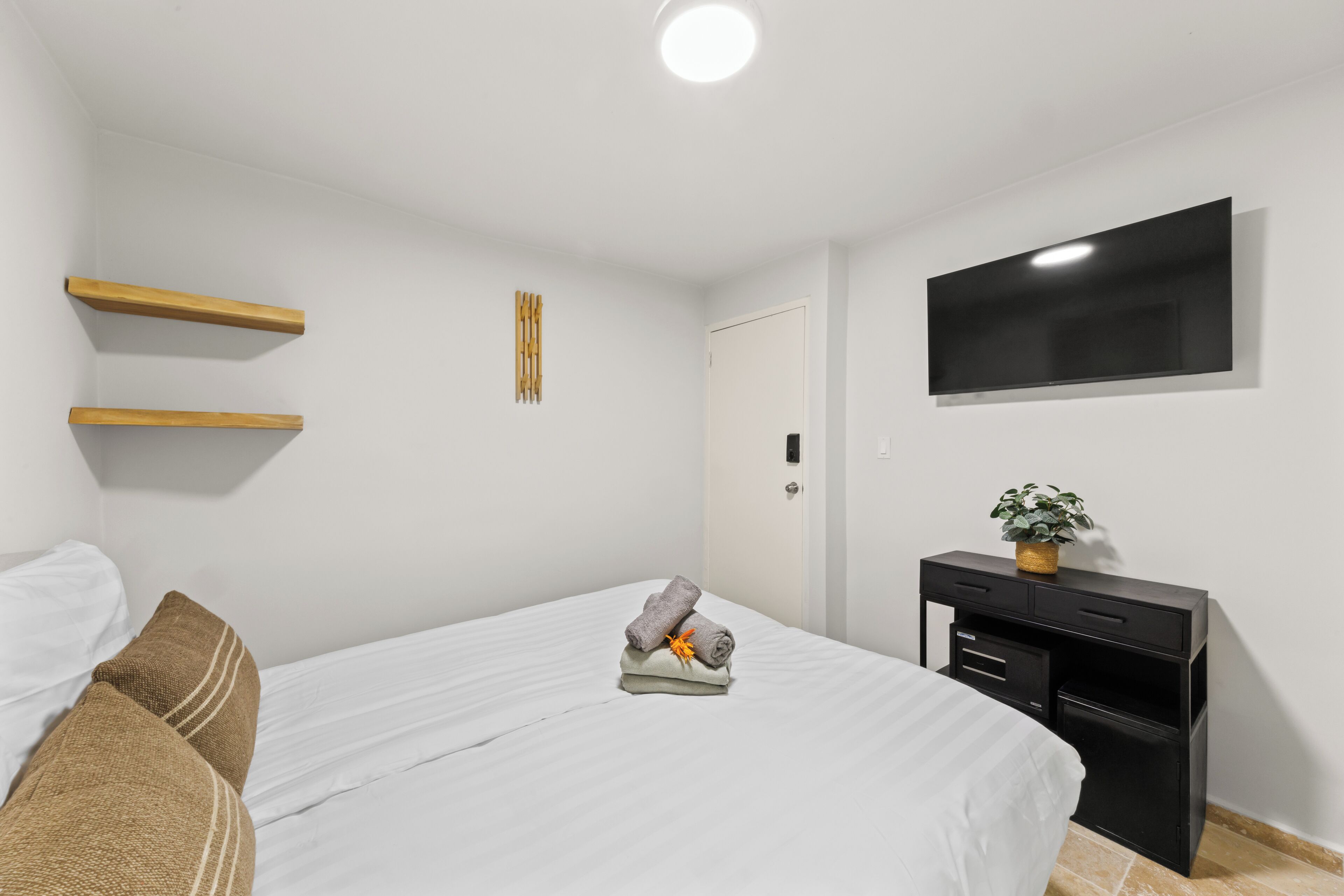 A hotel room with a bed, a desk, a TV, and a door.