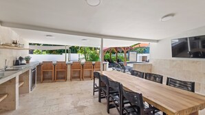 Een buitenkeuken met een eettafel, stoelen en een barbecue.