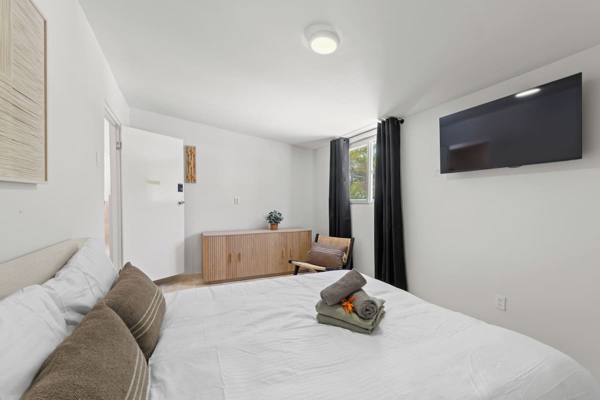 A modern hotel room with a large bed, a flat-screen TV mounted on the wall, a wooden cabinet, and a window with curtains.