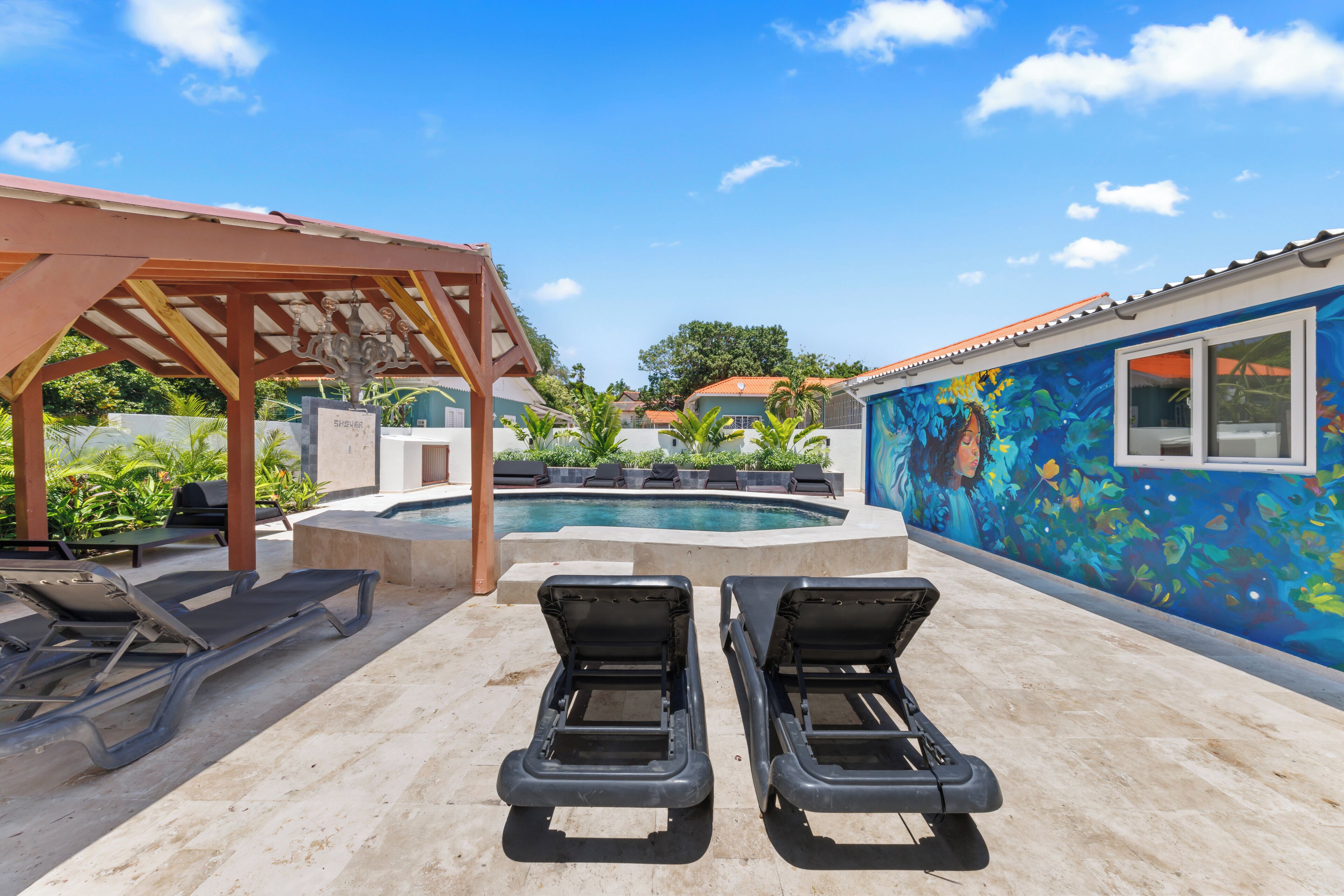 Ein Poolbereich mit Liegestühlen, einer Pergola und einem Wandgemälde an der Nachbarwand.