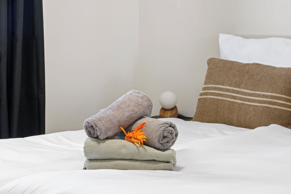 A neatly made bed with rolled towels and a decorative orange flower.