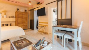 A hotel room with a bed, a wooden wardrobe, a TV mounted on the wall, a dining table with chairs, and a coffee table with remote controls. - Apartment 'Sublime Centre D’aix' with Shared Terrace, Wi-Fi and Air Conditioning (Aix-en-Provence)