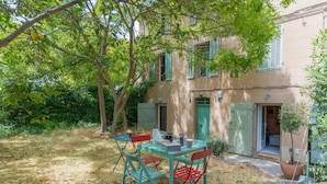 A patio with a table and chairs, a potted plant, and a building with green shutters. - Apartment 'Sublime Centre D’aix' with Shared Terrace, Wi-Fi and Air Conditioning (Aix-en-Provence)