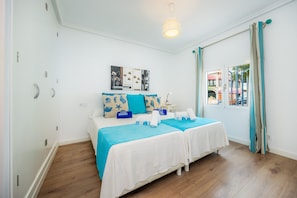 Una habitación con dos camas, una mesita de noche, una lámpara de techo y una ventana con cortinas.