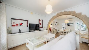 Een moderne woonkamer met een bank, een salontafel, een televisie en een stenen boog die leidt naar een eetgedeelte.