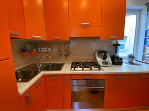 A kitchen with orange cabinets, stainless steel appliances, and a window with a view.