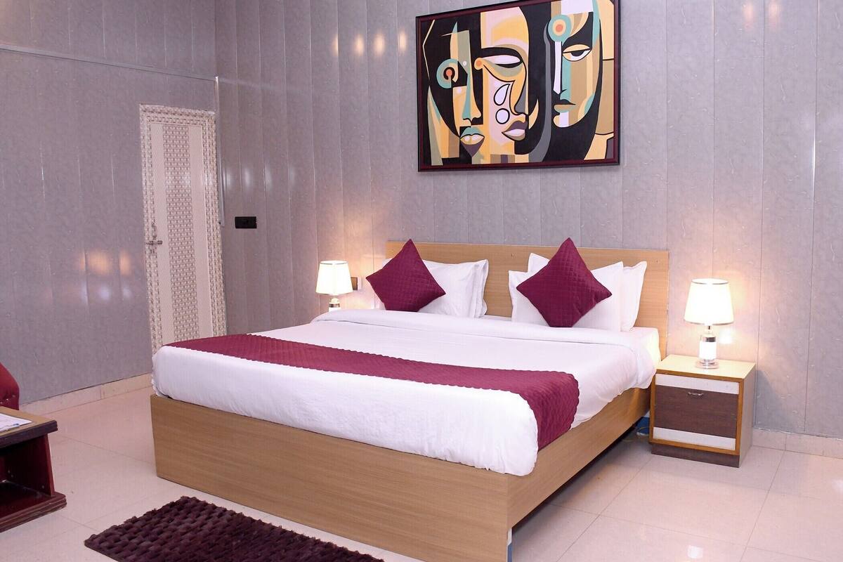 Una habitación de hotel moderna con una cama grande, dos mesitas de noche con lámparas, un cabecero de madera y un cuadro abstracto de gran tamaño en la pared.