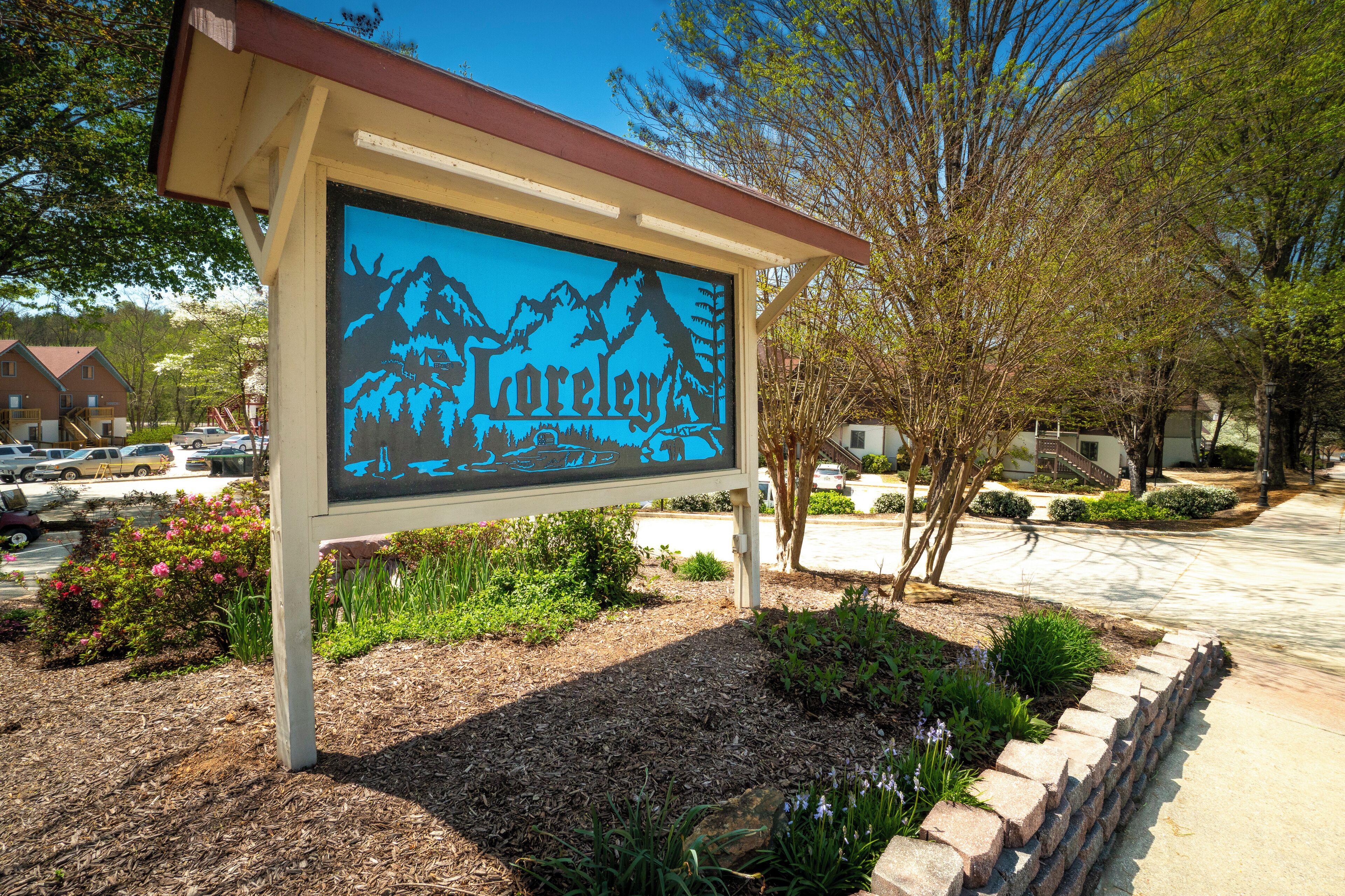 A sign with the name 'Lorelai' and a mountain graphic, surrounded by landscaping and a parking area.
