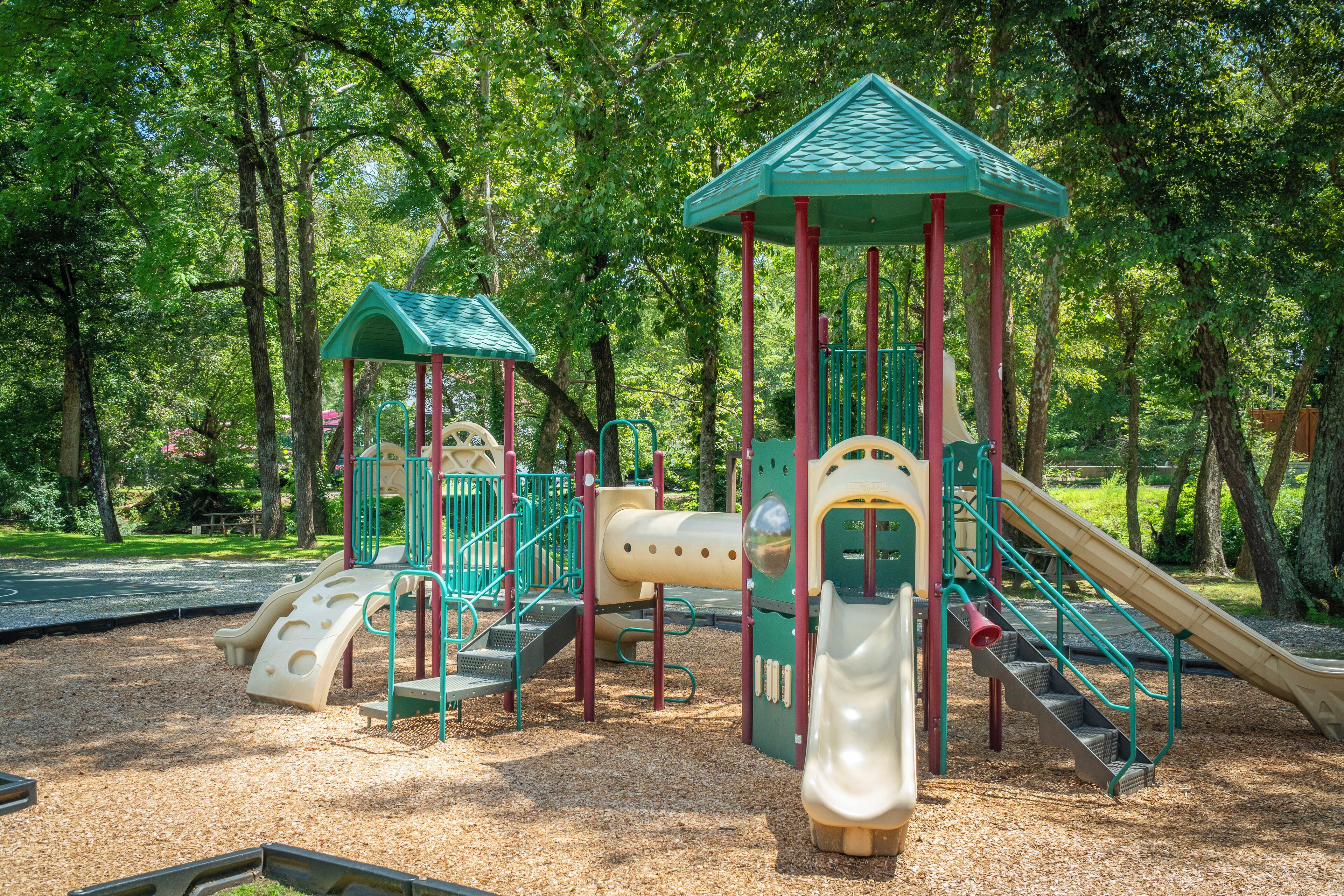 A playground with slides and climbing structures surrounded by trees.