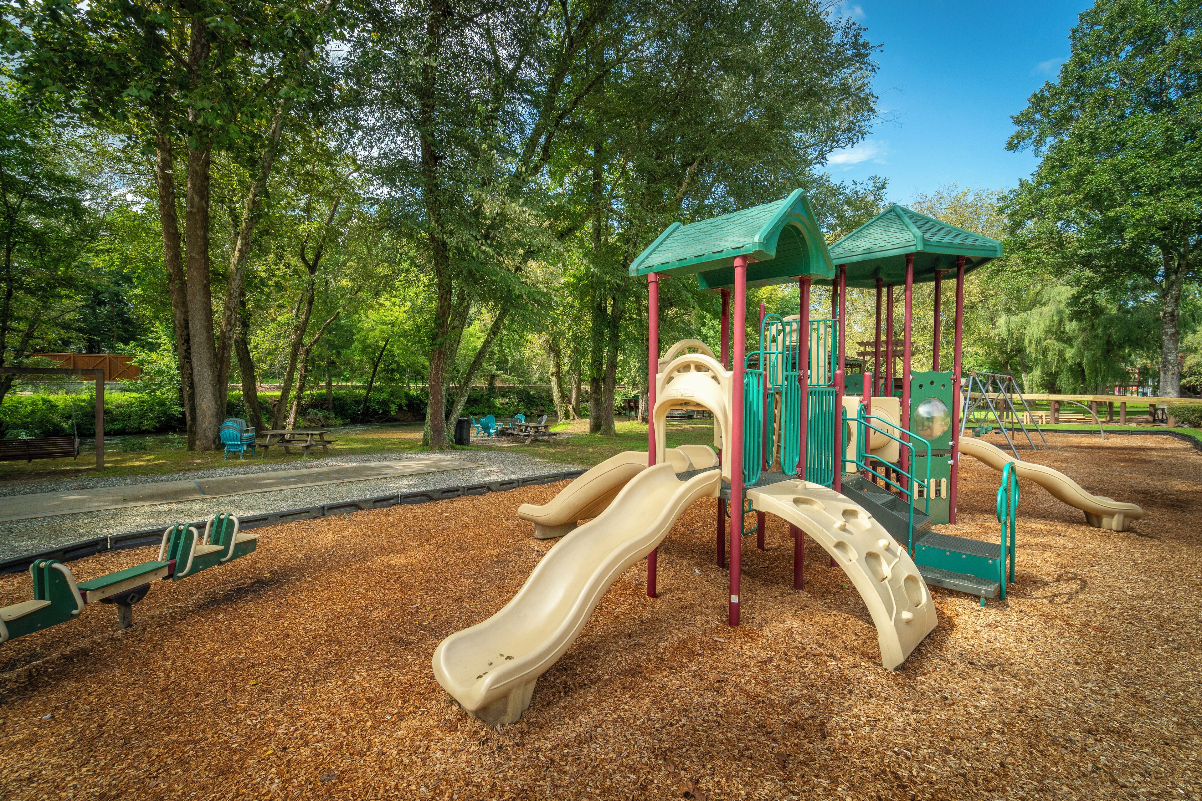 Un parque infantil con toboganes y estructuras para escalar, rodeado de árboles.