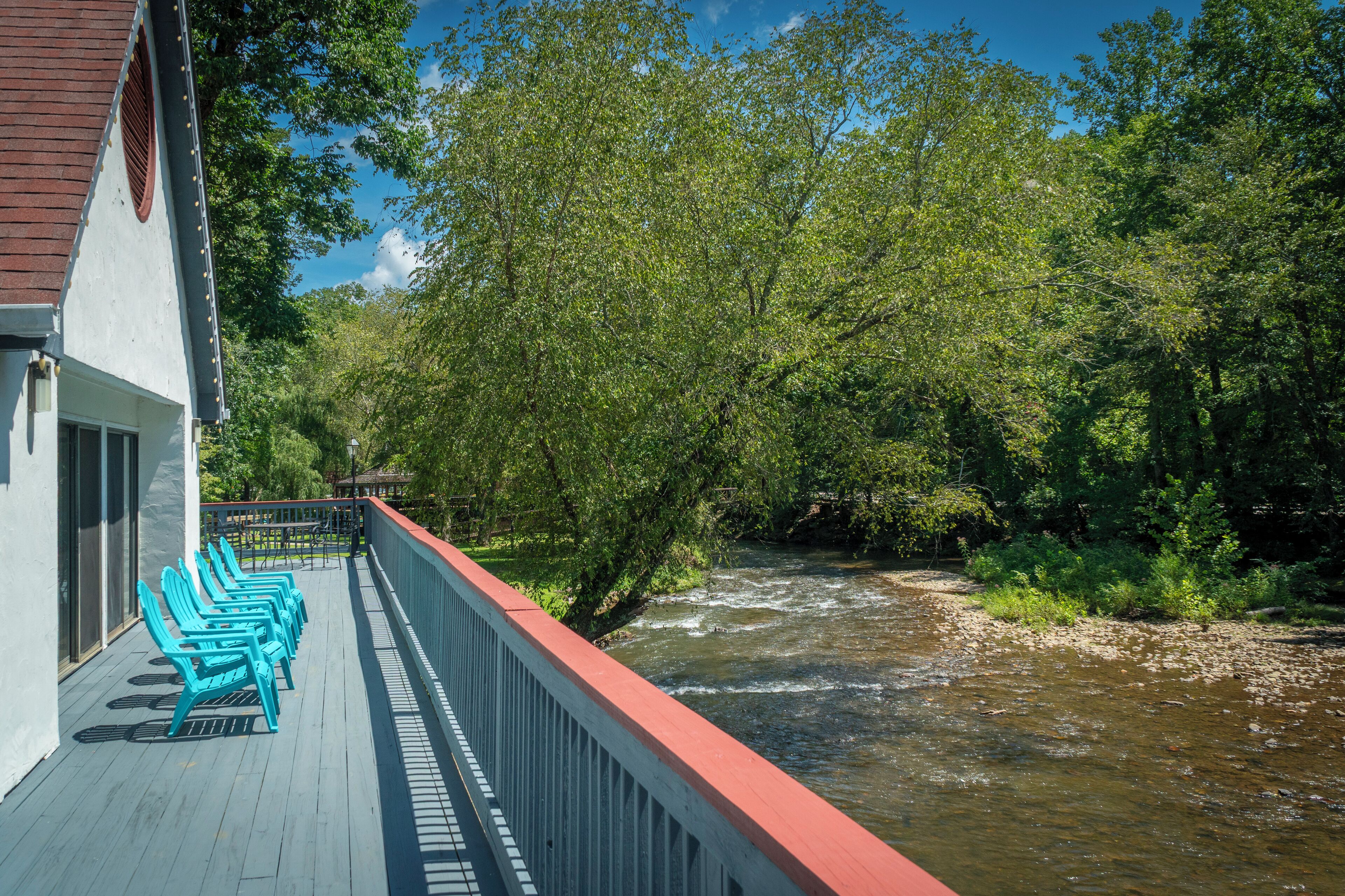 A wooden deck with blue chairs and a railing overlooking a river.