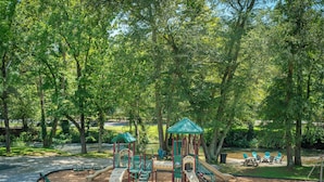 Un parque infantil con toboganes y estructuras para escalar, rodeado de árboles.