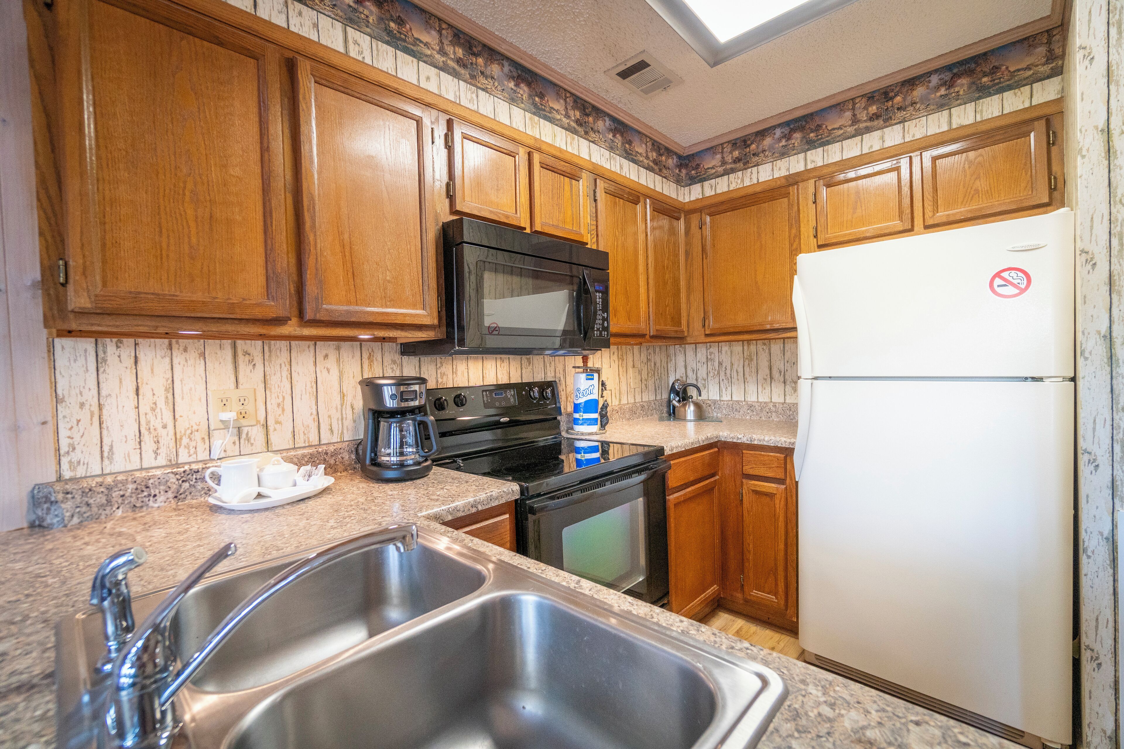 A kitchen with wooden cabinets, a microwave, a stove, a sink, and a refrigerator.