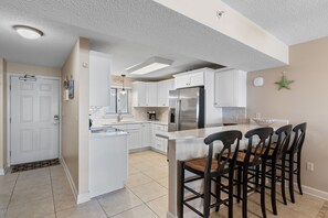 A modern kitchen with white cabinetry, a stainless steel refrigerator, and a breakfast bar with wooden chairs.