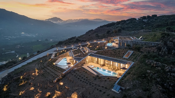 A modern resort with a swimming pool, terraced gardens, and a mountainous backdrop. - Neromai Cave Luxury Villa One (Rethymno)