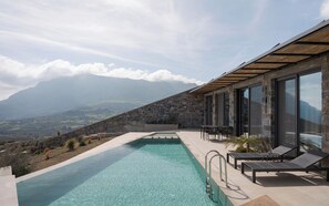 Un espace piscine offrant une vue dégagée sur les montagnes, agrémenté de murs en pierre et de mobilier d’extérieur moderne.
