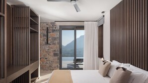 Une chambre avec un lit, des étagères en bois, un mur en pierre, un ventilateur de plafond et une vue sur les montagnes.