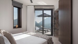 Une chambre avec un grand lit, une fenêtre et une vue sur un balcon aménagé avec du mobilier d’extérieur.