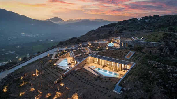 A modern resort with a swimming pool, terraced gardens, and a mountainous backdrop.