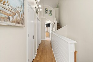 Un couloir doté d’un plancher en bois, de murs blancs et d’un escalier avec une rampe blanche.