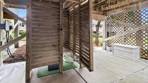 A wooden structure with a slatted roof, concrete flooring, and a lattice fence in the background.