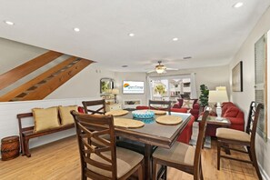 A spacious living area with a dining table, chairs, and a staircase. - Dog-Friendly 3BR · Gulf Beach Steps Away· Sleeps 9 (Port St. Joe)