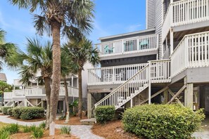 A beachfront hotel with multiple balconies, palm trees, and a wooden walkway.