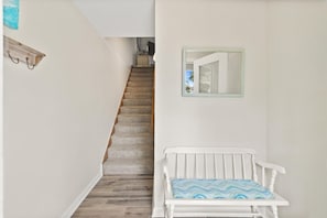 Eine Treppe führt zu einer oberen Etage, eine weiße Bank mit gemustertem Kissen und ein Spiegel an der Wand.