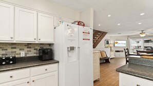 A kitchen with white cabinets, a refrigerator, a coffee maker, and a staircase leading to a balcony.